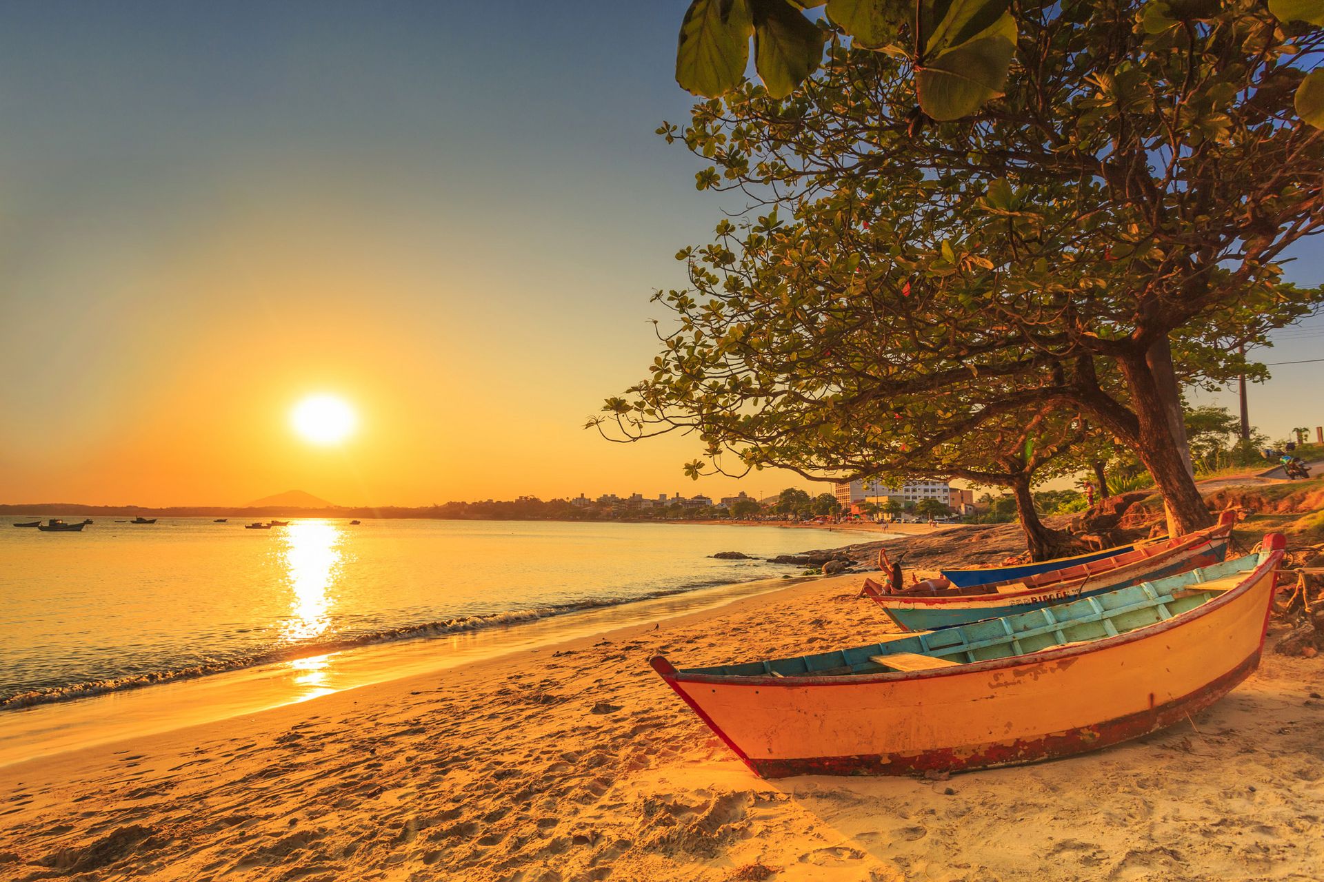 Pôr do sol na Praia de Meaípe, em Guarapari, com barcos de pesca na areia e o mar calmo alaranjado