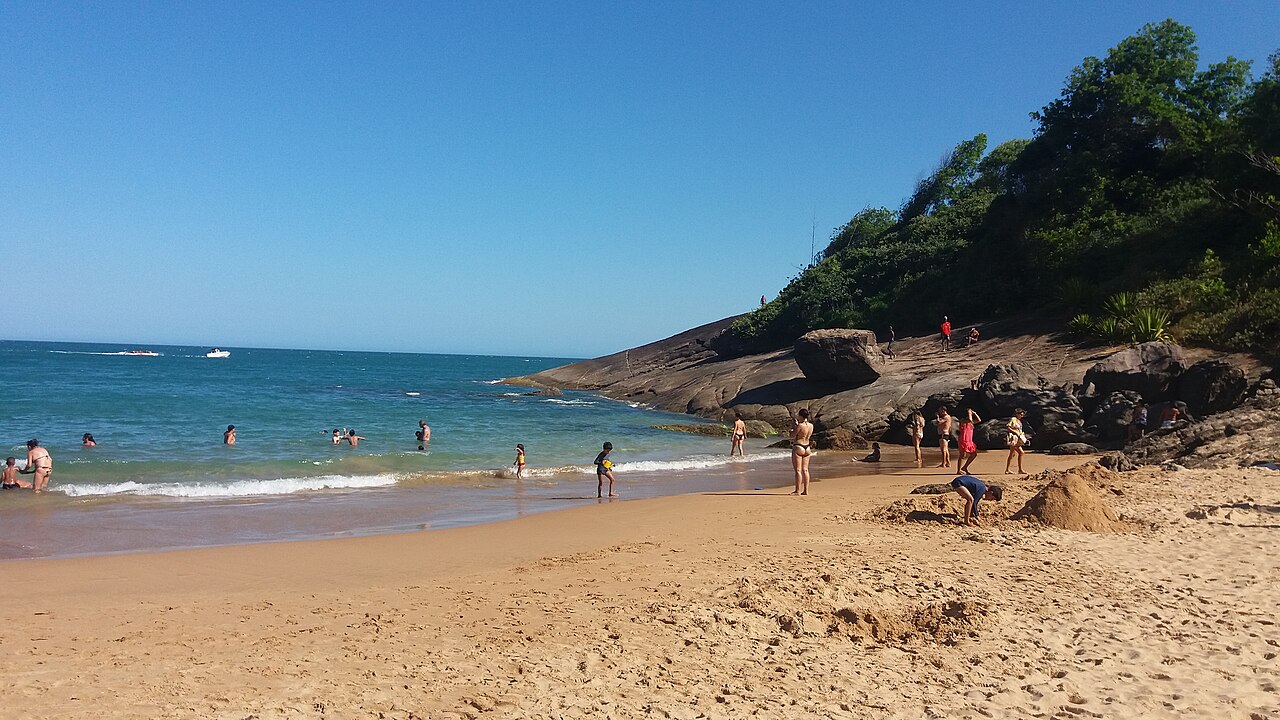 Praia dos Padres: pequena enseada de areia rodeada por pedras e vegetação, com banhistas