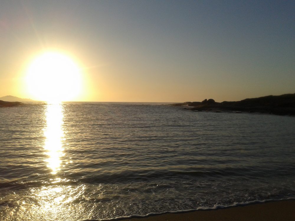 Praia do Ermitão ao pôr do sol, cercada de vegetação