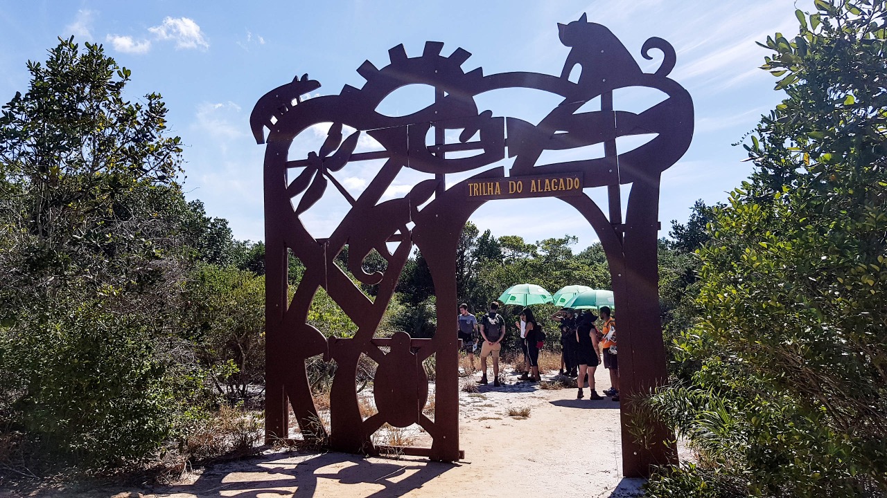 Portal de entrada da Trilha do Alagado no Parque Estadual Paulo César Vinha, com visitantes ao fundo